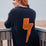 Person wearing a black sweater with an orange lightning bolt design, standing on a wooden deck by the sea.