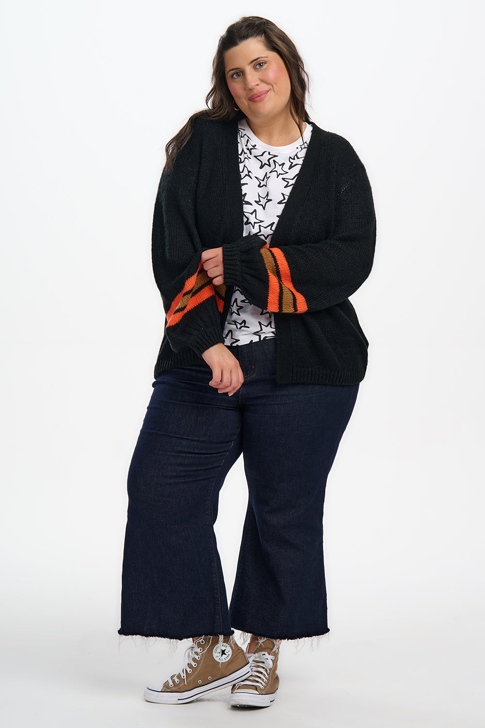 Woman wearing a black cardigan, navy pants, and white sneakers on a white background