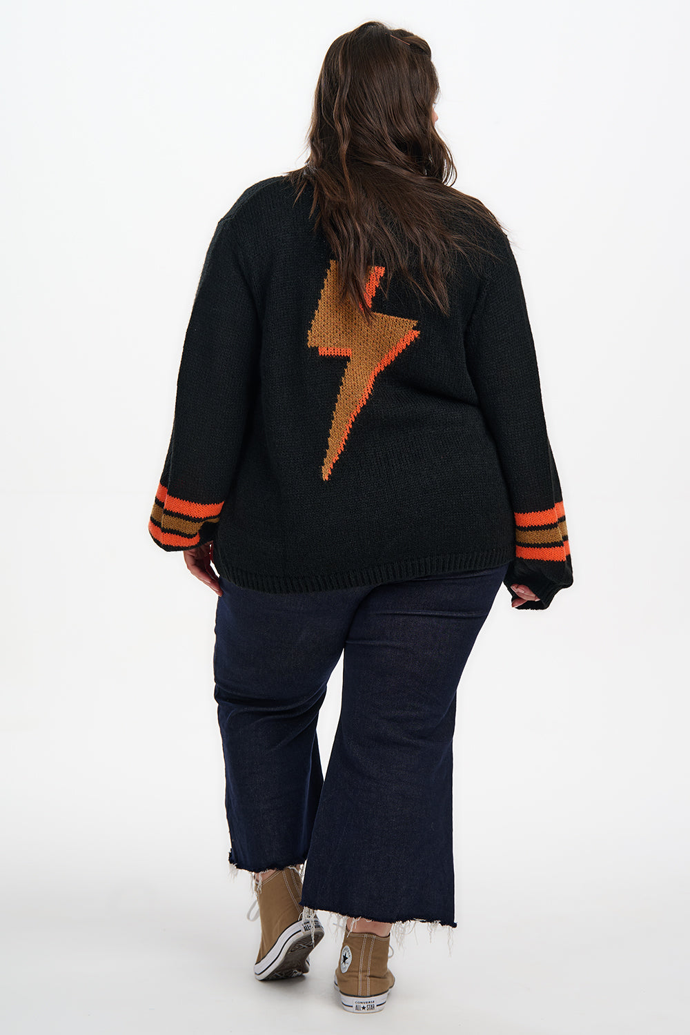Person wearing a black sweater with an orange lightning bolt design on the back, standing against a white background.
