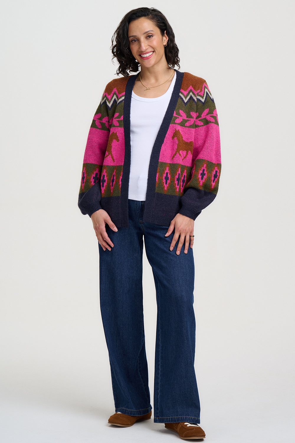Woman wearing a colorful patterned cardigan over a white shirt and blue jeans on a white background