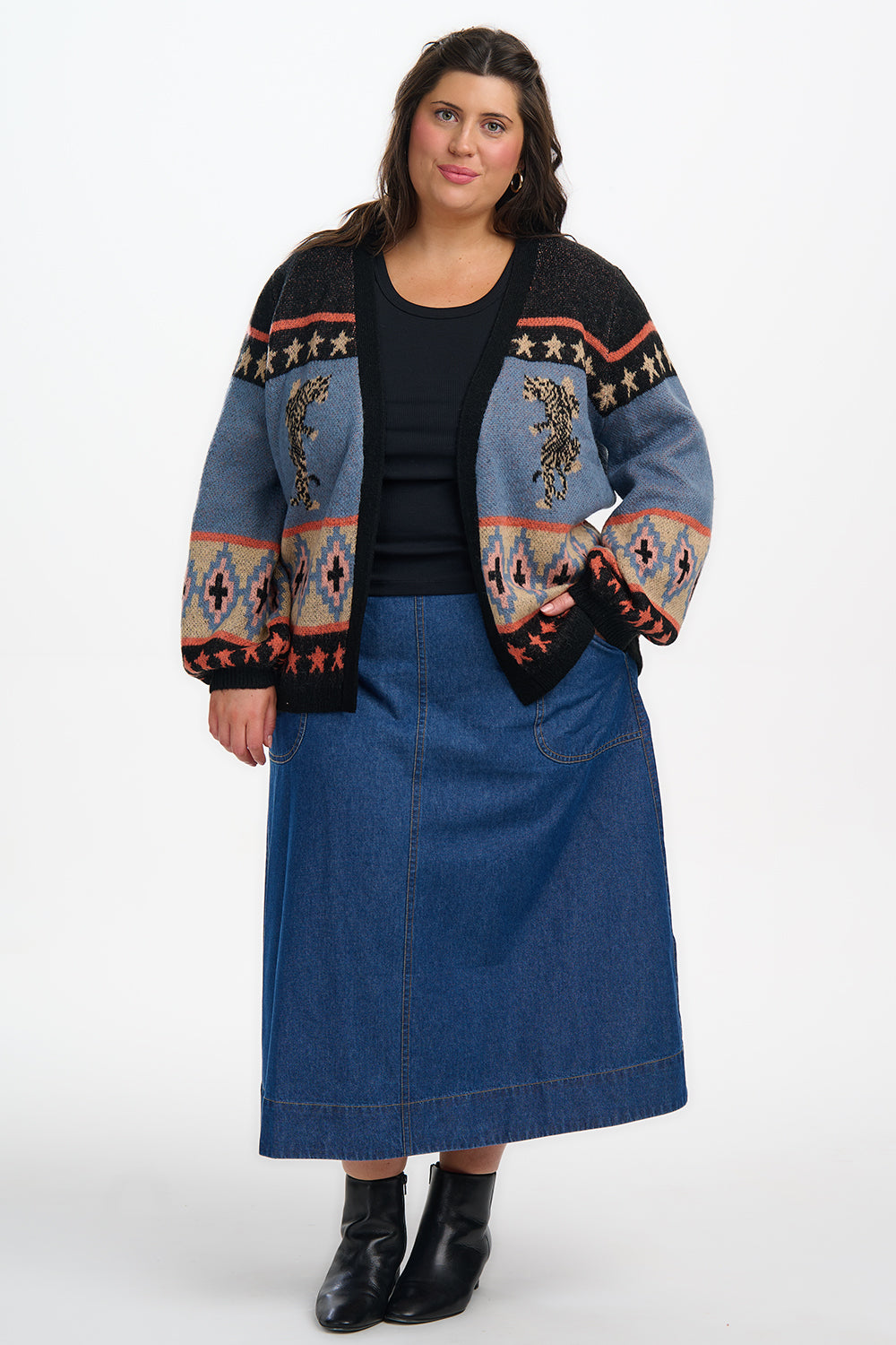 Woman wearing a patterned cardigan over a black top and blue denim skirt on a white background