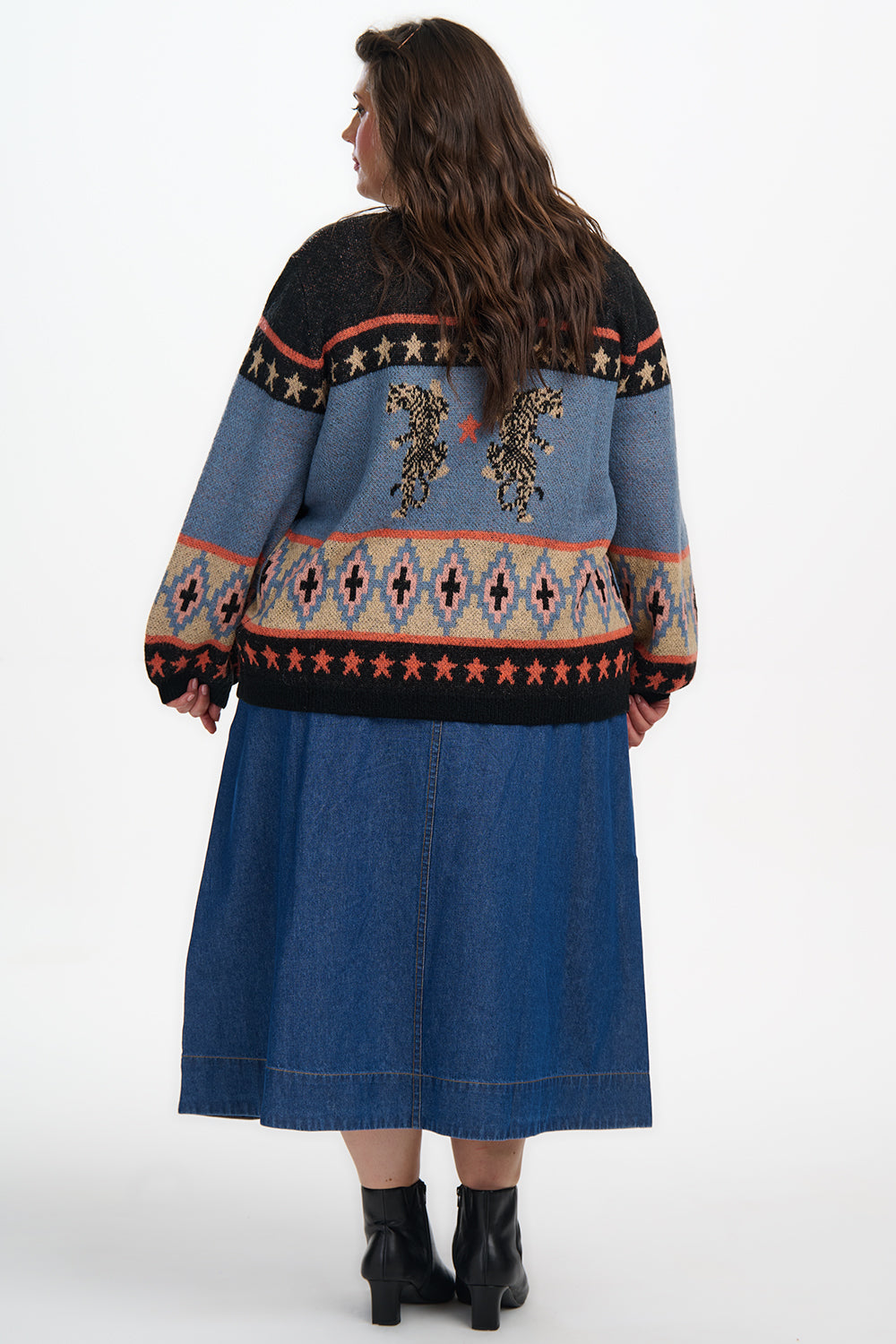 Person wearing a blue patterned sweater and denim skirt on a white background