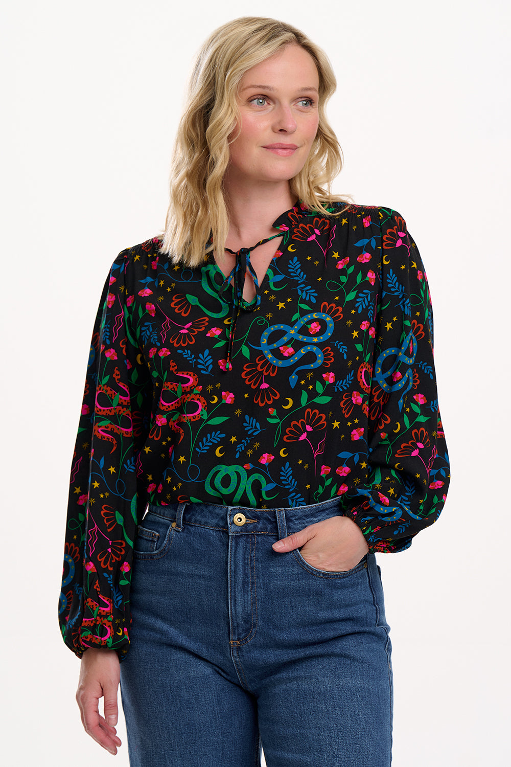 Woman wearing a colorful patterned blouse with blue jeans on a white background