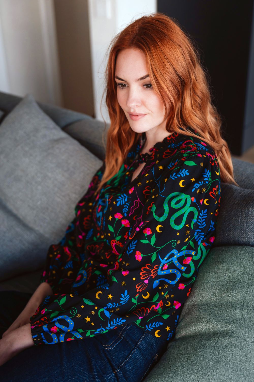 Woman sitting on a couch wearing a colorful embroidered shirt.