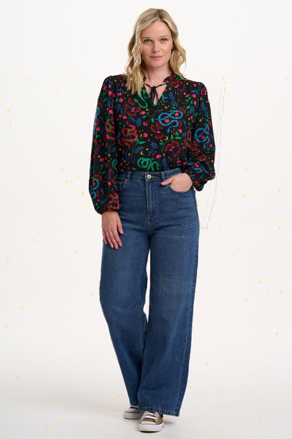 Woman wearing a colorful patterned blouse and blue jeans on a white background