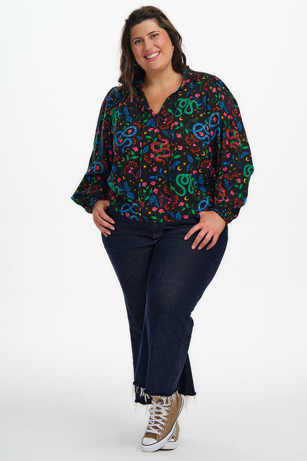 Woman wearing a colorful patterned blouse and dark jeans on a white background