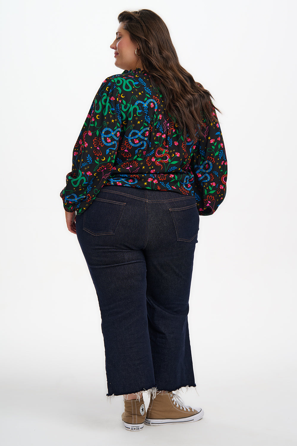 Person wearing a colorful patterned jacket and dark jeans on a white background