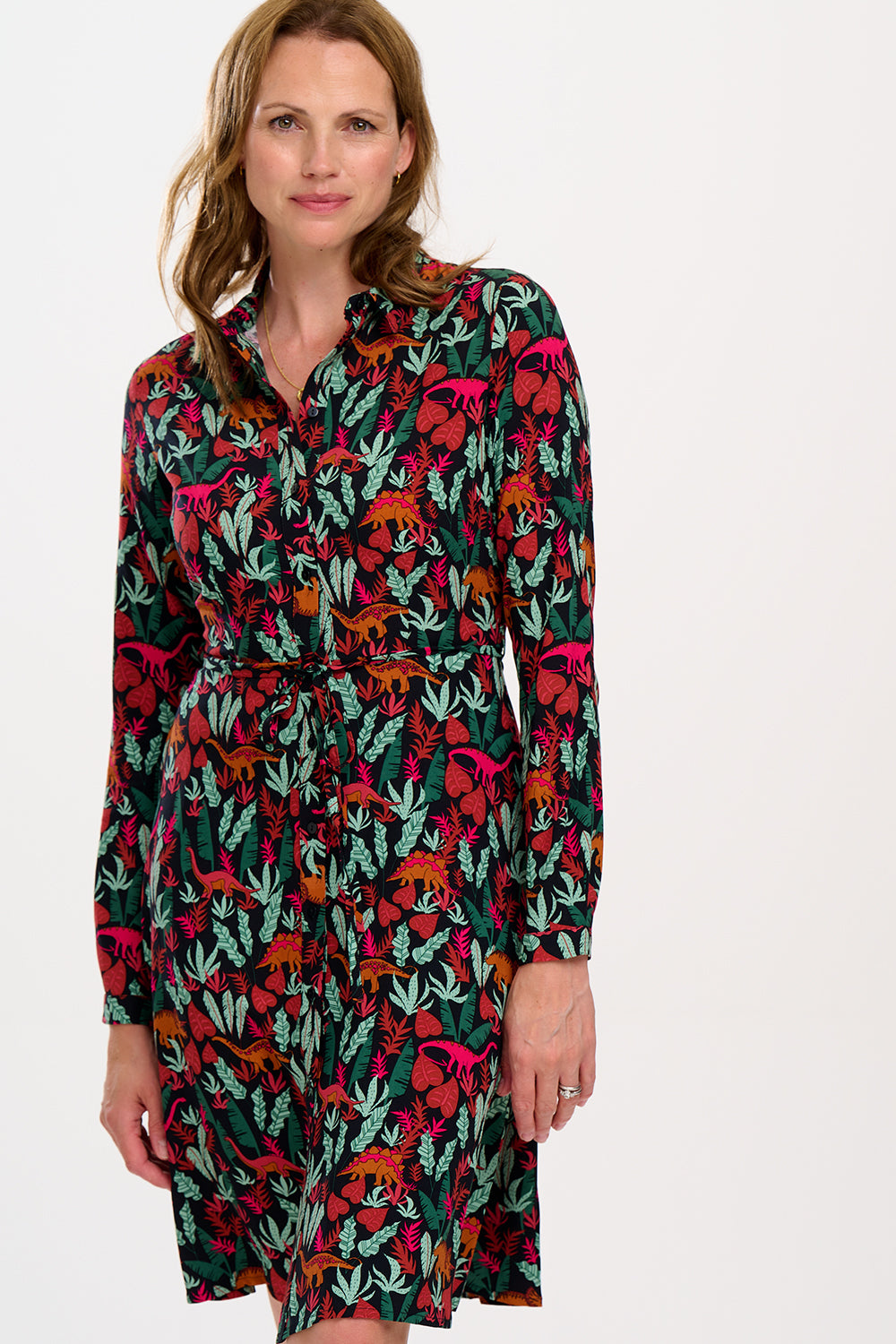 A woman wearing a black, floral shirt dress with a tie waist belt and relaxed collar.