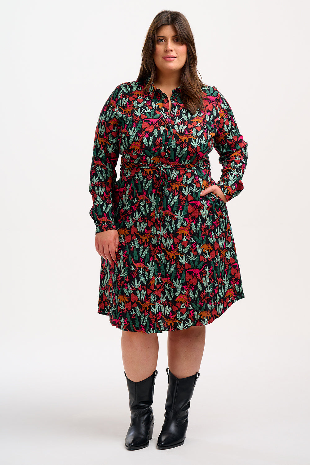 A woman wearing a black, floral shirt dress with a tie waist belt and relaxed collar.
