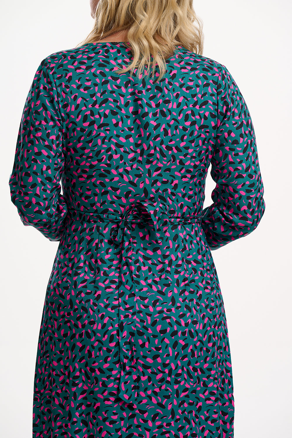 Person wearing a teal dress with pink pattern, standing against a white background