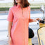 Woman in a pink dress standing next to a yellow scooter on a street.