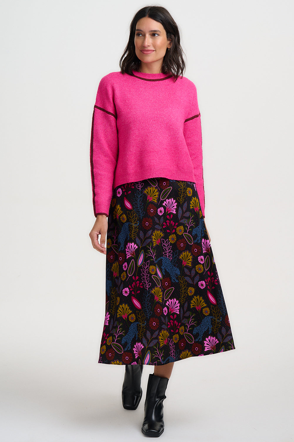 Woman wearing a bright pink sweater and a dark floral skirt on a white background