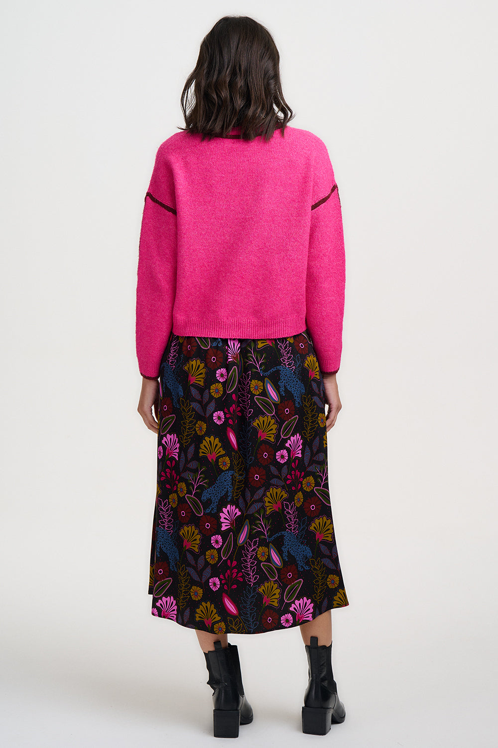 Person wearing a bright pink sweater and a colorful floral skirt on a white background