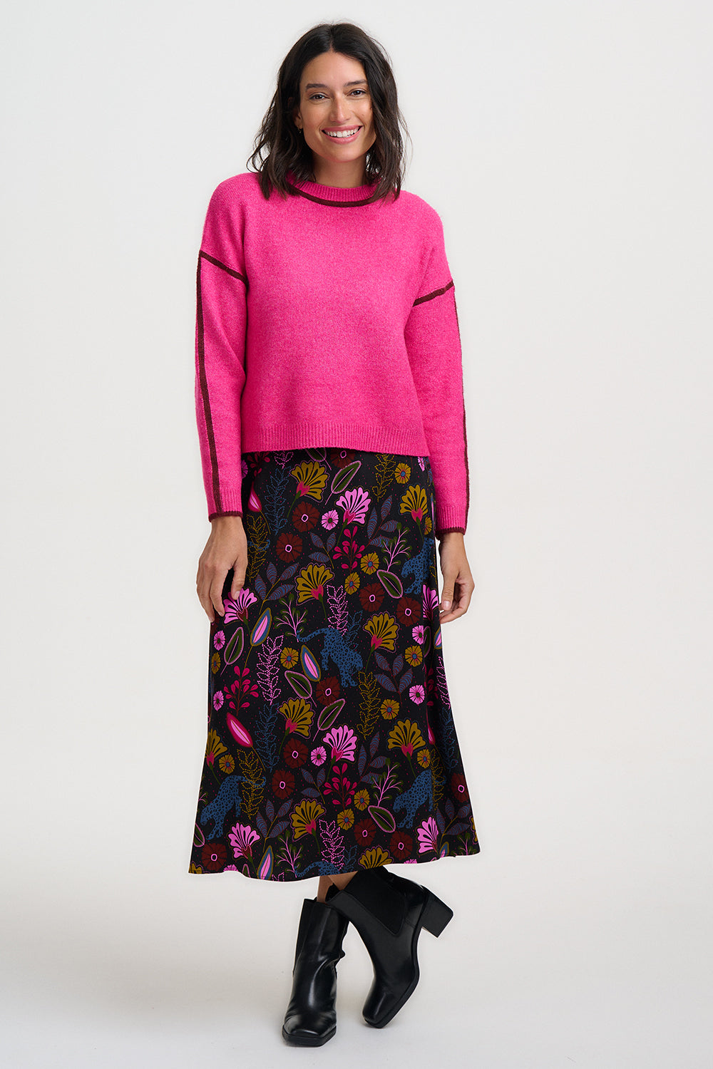 Woman wearing a bright pink sweater and a colorful floral skirt on a white background