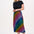 A woman standing and wearing a high-waisted, midi-length Zora skirt with a Rainbow Checkerboard design on a black base.