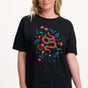 Woman wearing a black t-shirt with a colorful snake and floral design on a plain background