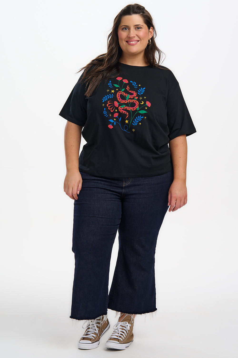 Person wearing a black t-shirt with a colorful design and dark jeans on a white background