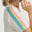 Woman wearing a white top with rainbow-colored straps on a plain background