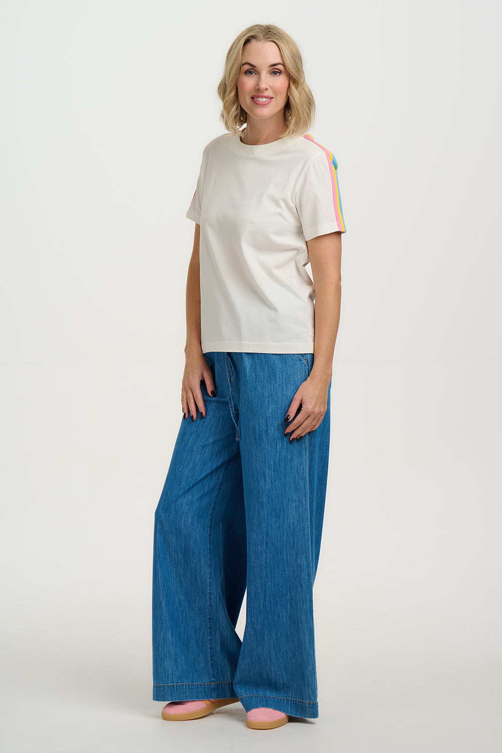 Woman wearing a white t-shirt with colorful sleeves and blue jeans on a white background