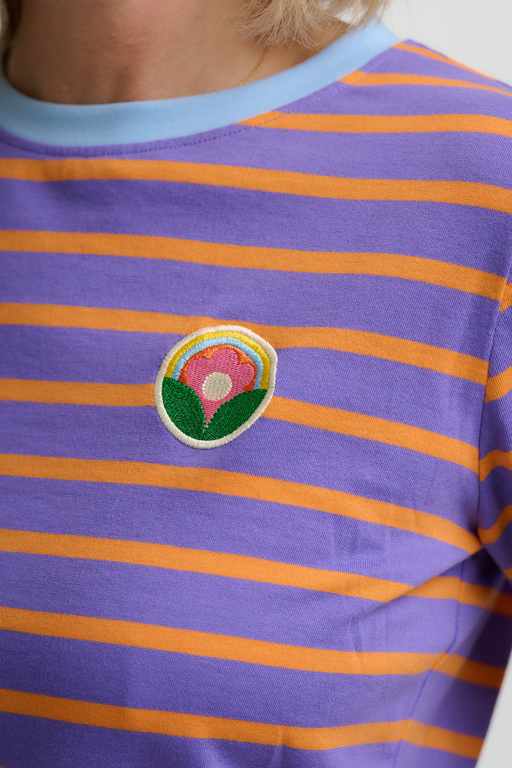 Purple and orange striped shirt with a floral patch on a white background