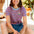 Woman wearing a striped shirt with a logo and denim shorts, sitting outdoors.