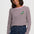 A woman wearing a long-sleeve crop top with dark red and white horizontal stripes, a light pink crew neck, and a small embroidered green duck on the chest, paired with dark blue jeans against a light gray background.