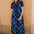 Woman wearing a blue floral dress standing against a beige wall.