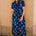 Woman wearing a blue floral dress standing against a beige wall.