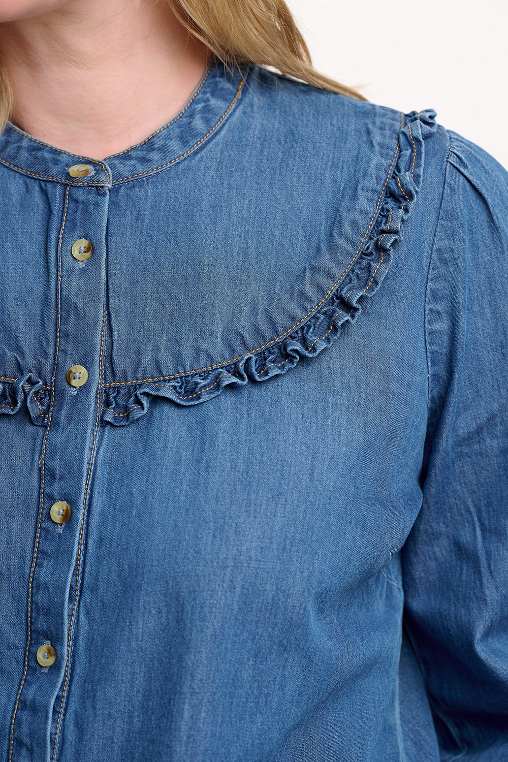SClose-up of a blue denim shirt with ruffled collar and buttons.