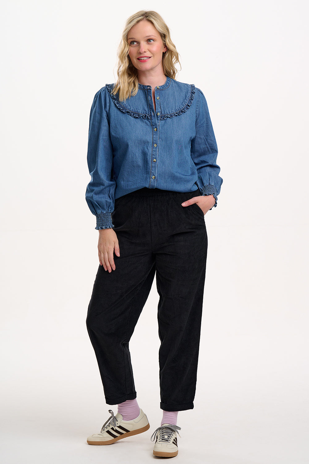 Sugarhill Brighton model wearing a blue denim shirt and black pants on a white background
