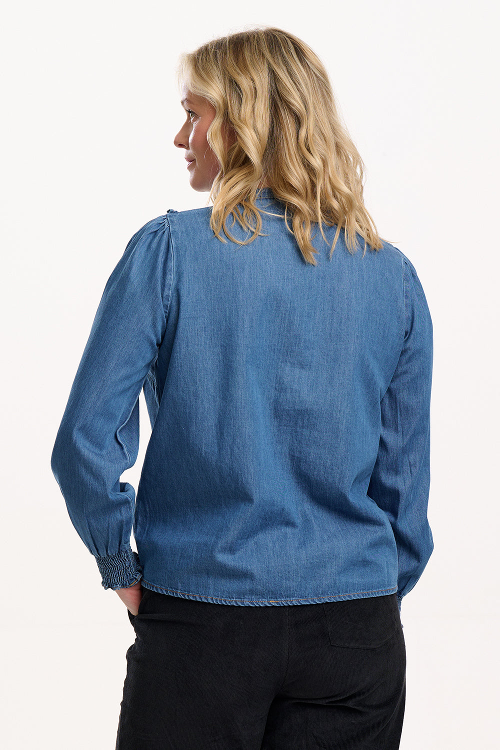 Sugarhill Brighton wearing a blue denim shirt on a white background