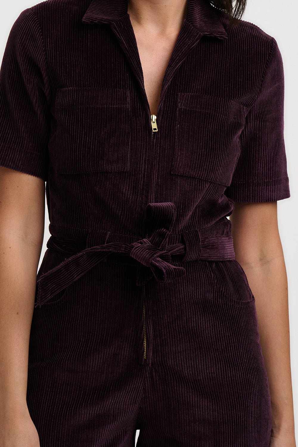 Purple corduroy jumpsuit worn by a person on a white background