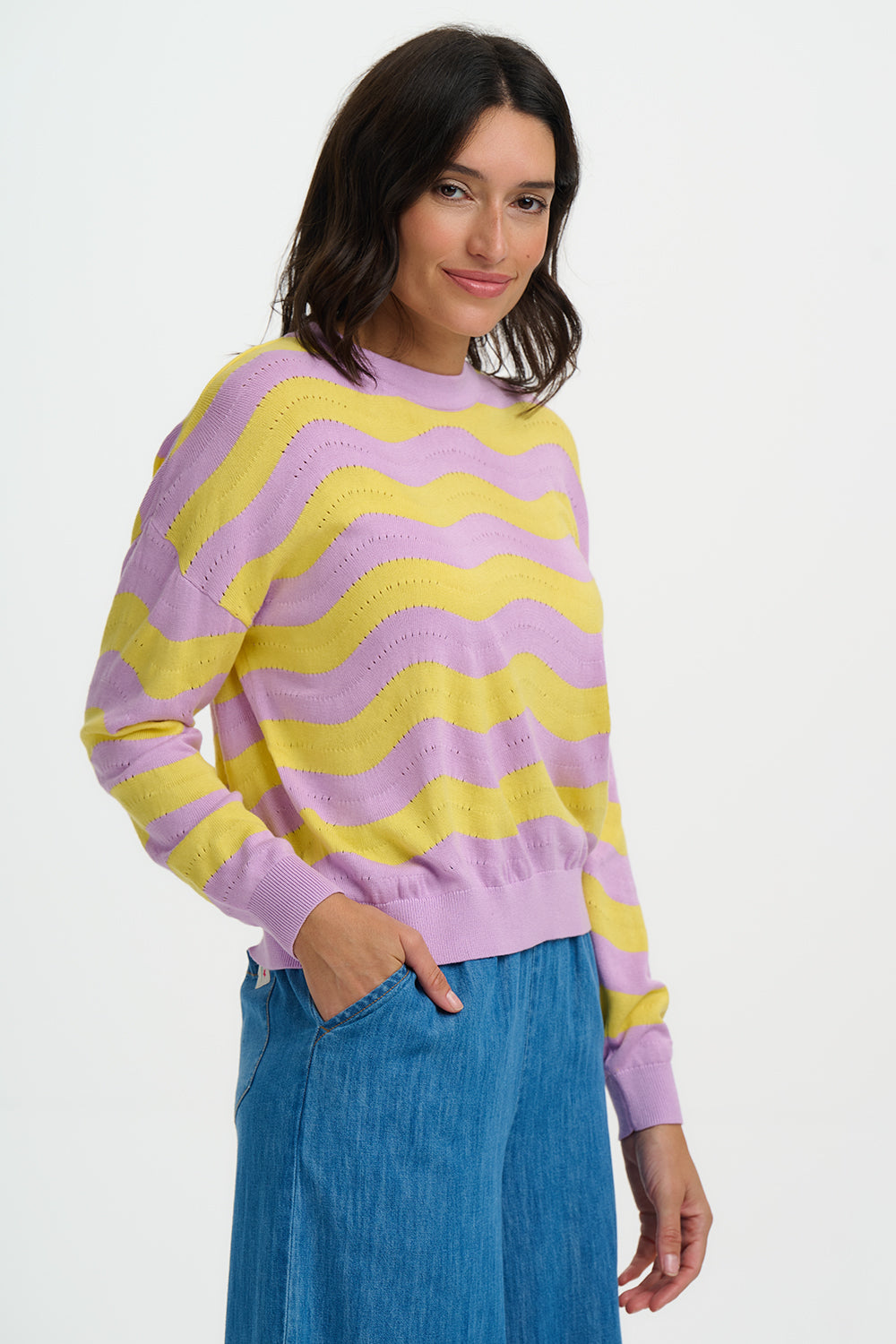 Woman wearing a purple and yellow striped sweater with blue jeans on a white background