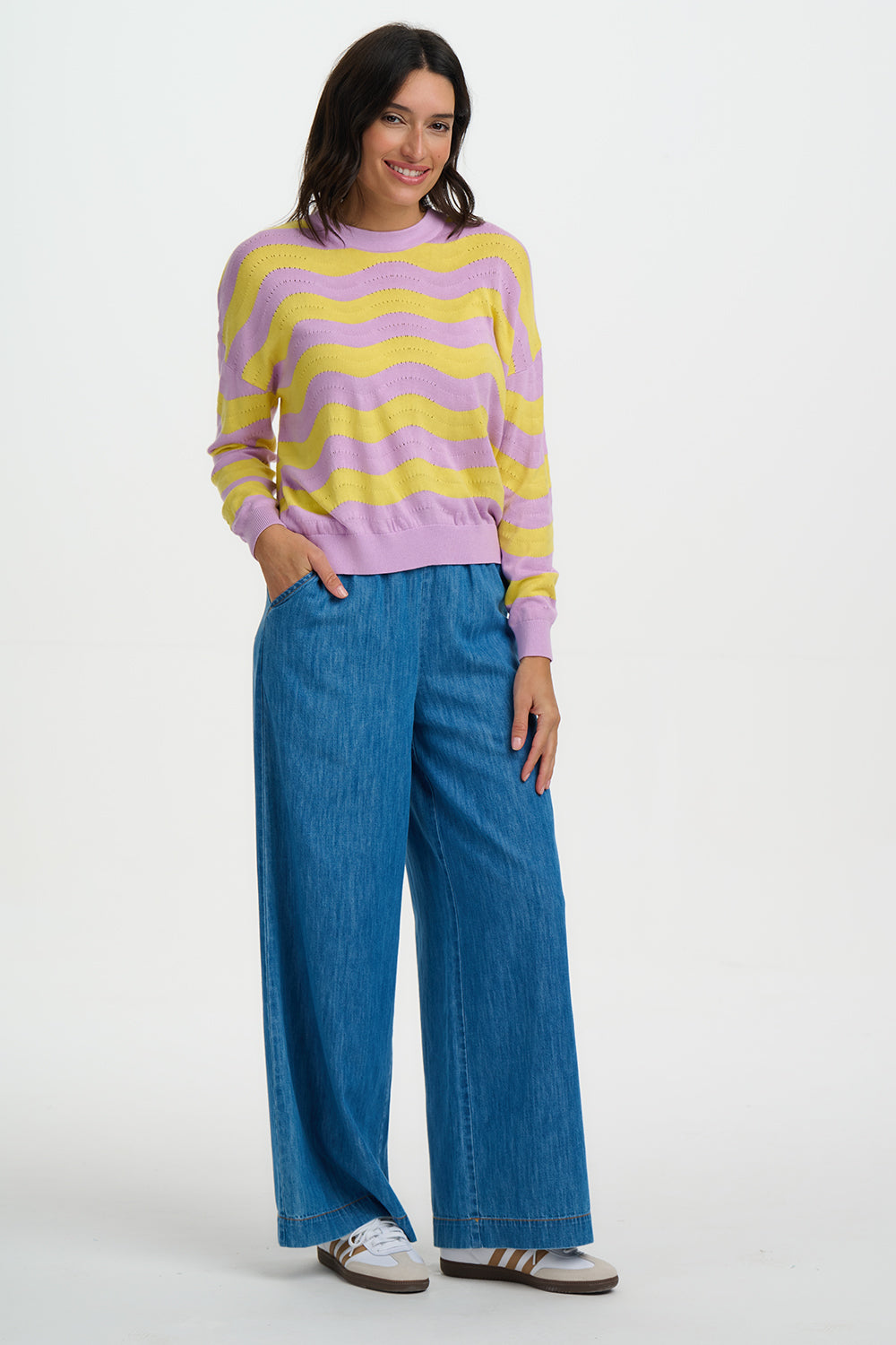 Woman wearing a colorful striped sweater and blue jeans on a white background