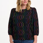 Sugarhill Brighton model wearing a black blouse with a colourful pattern on a white background