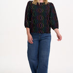 Sugarhill Brighton model wearing a black patterned top and blue jeans on a white background