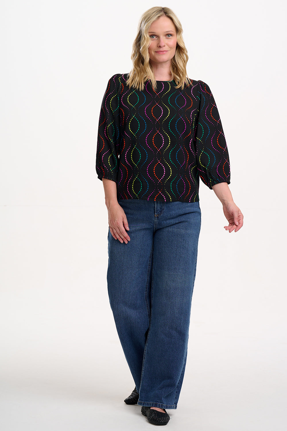 Sugarhill Brighton model wearing a black patterned top and blue jeans on a white background