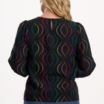 Sugarhill Brighton model wearing a black blouse with colourful pattern on a white background