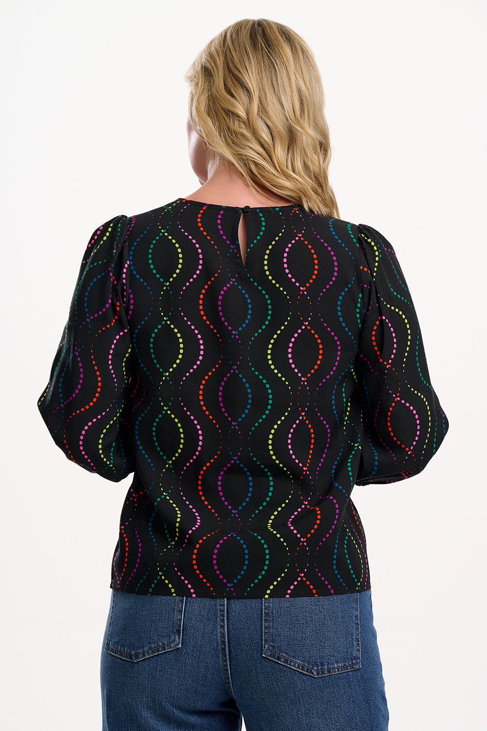 Sugarhill Brighton model wearing a black blouse with colourful pattern on a white background