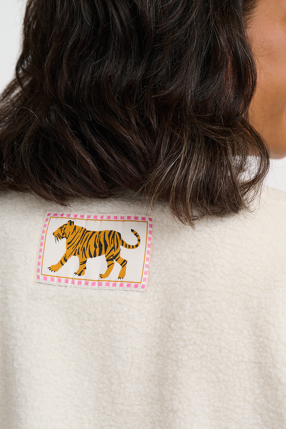 Close-up of the back of a person wearing a cream-colored textured sweater, featuring a rectangular patch with a yellow and black striped tiger on a pink patterned border.