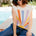 Woman wearing a colorful striped shirt and sunglasses sitting by a pool.