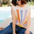 Woman wearing a colorful striped shirt and sunglasses sitting by a pool.