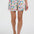 Woman wearing a white top with colorful trim and patterned shorts on a white background