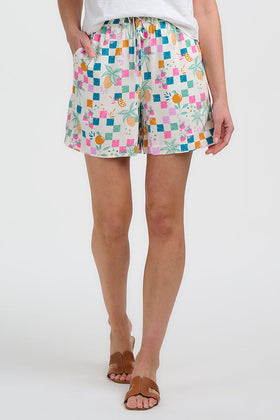 Woman wearing a white top with colorful trim and patterned shorts on a white background