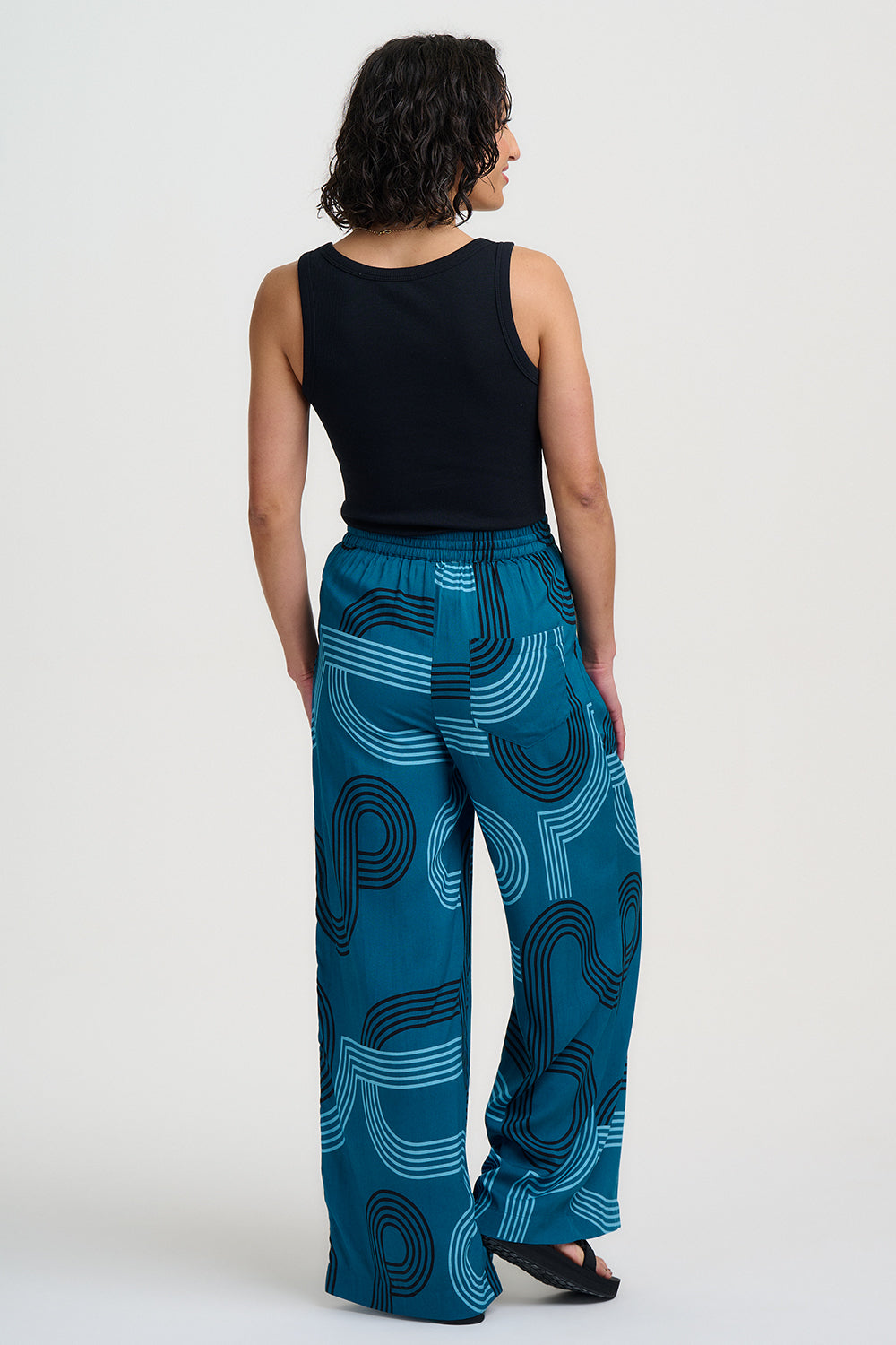 Woman wearing teal pants with a geometric pattern on a white background