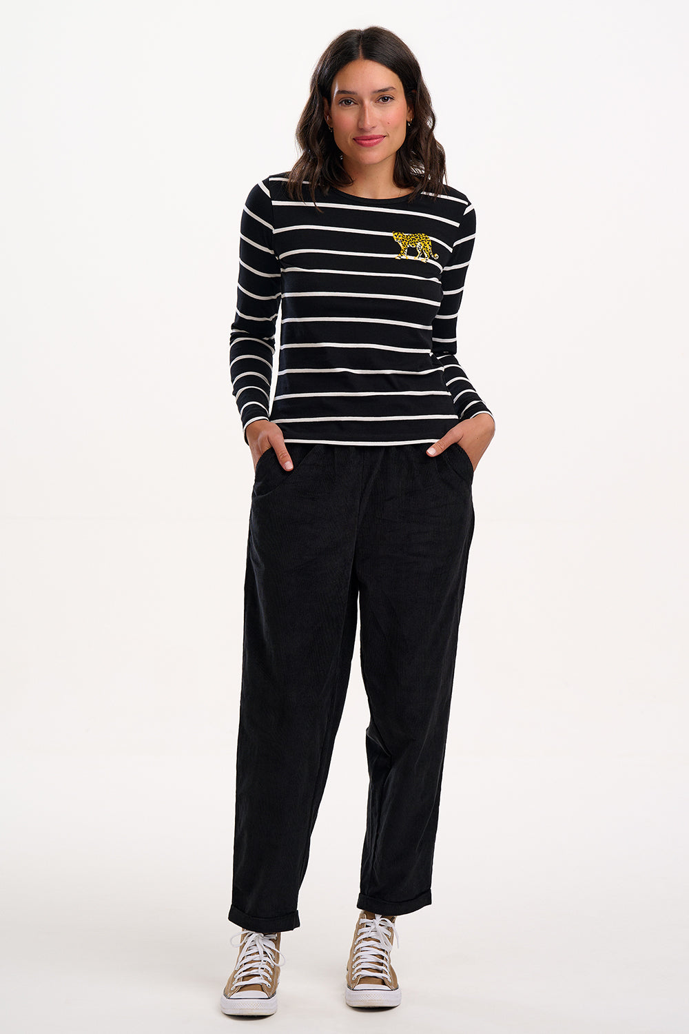 Woman wearing a black and white striped shirt with a logo and black trousers on a white background