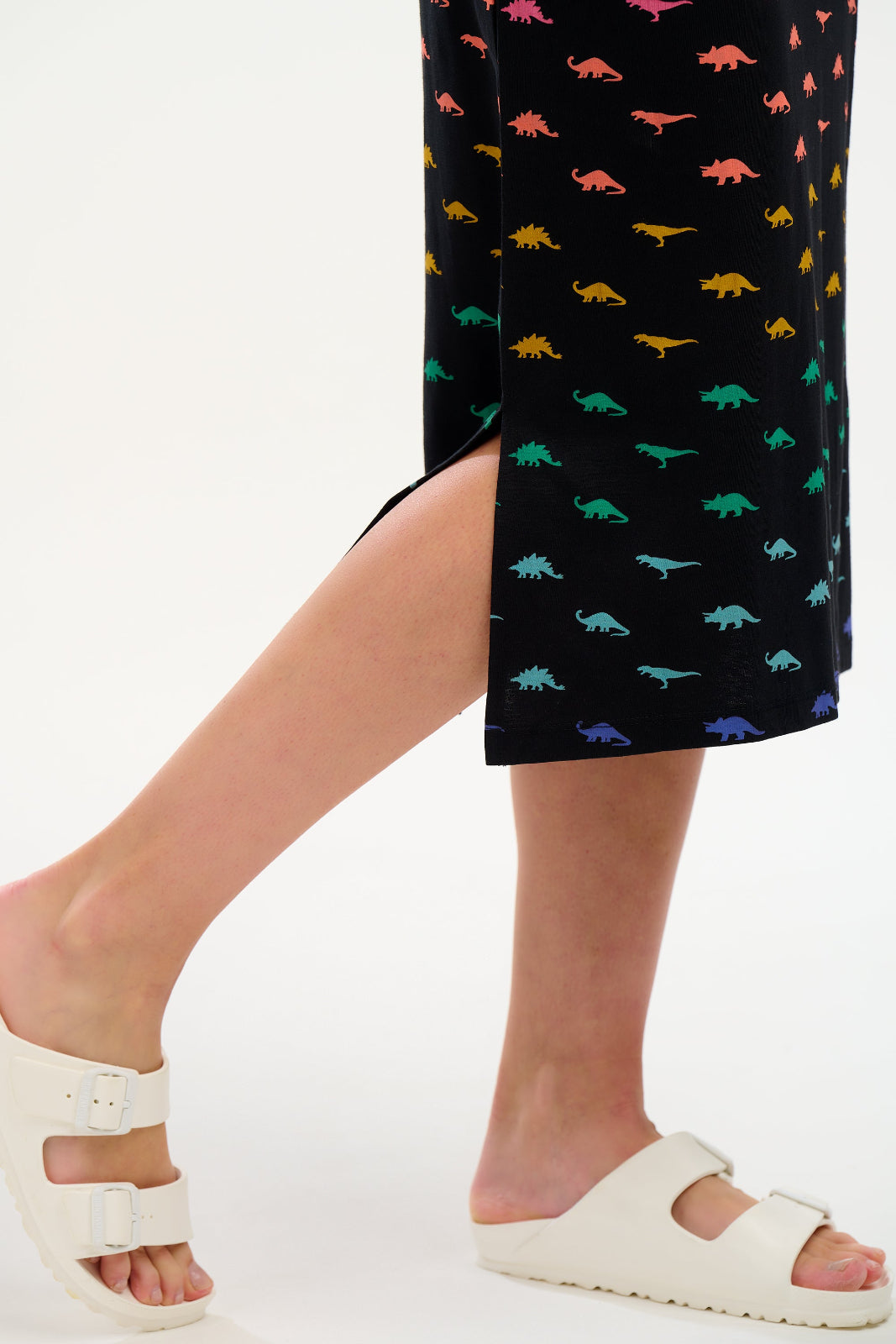 Person wearing a black skirt with colorful dinosaur pattern and white sandals on a white background