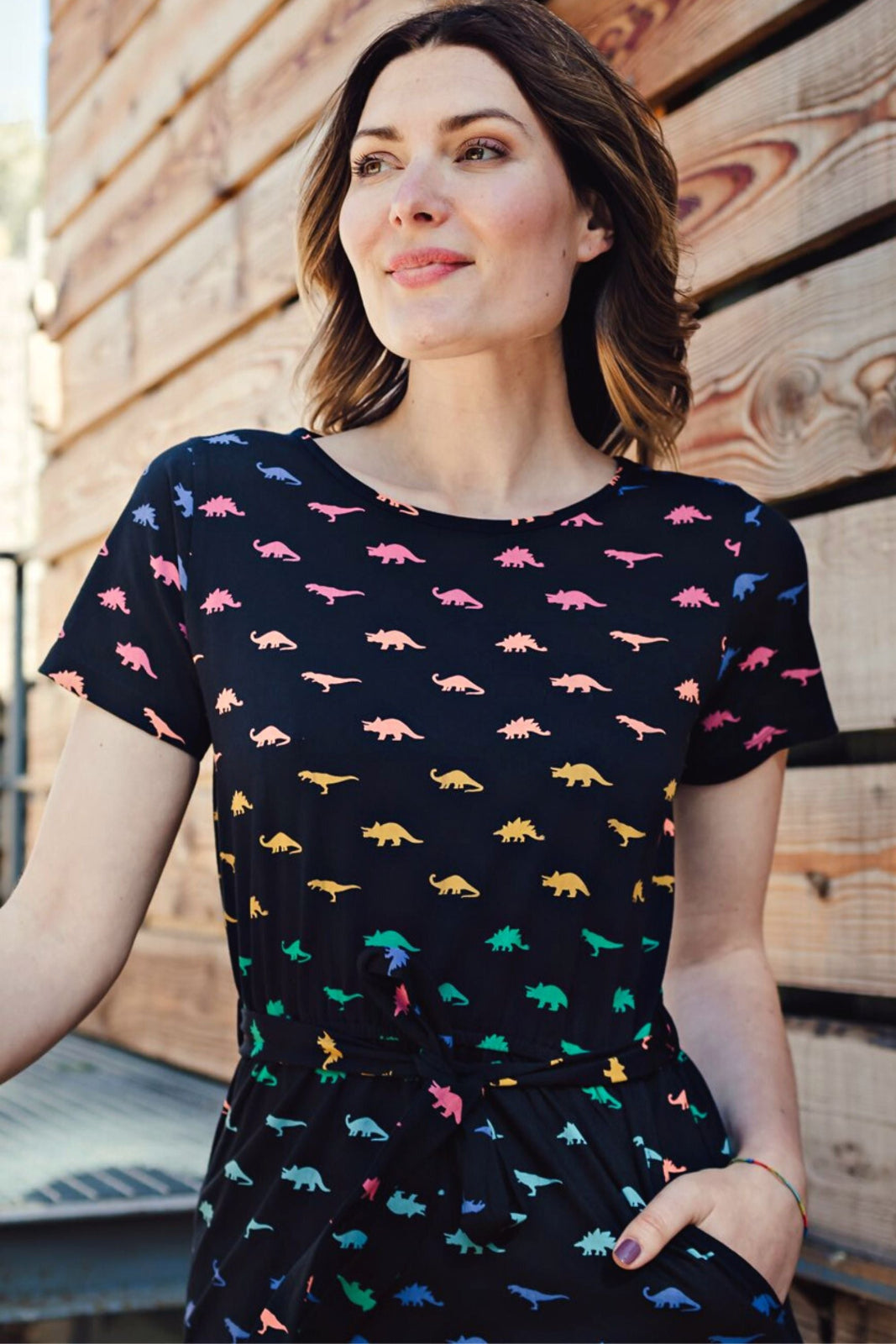 Woman wearing a black t-shirt with colorful dinosaur pattern against a wooden wall.