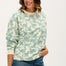 A woman wearing an oversized sweatshirt with a green leopard print on it, paired with blue jeans.