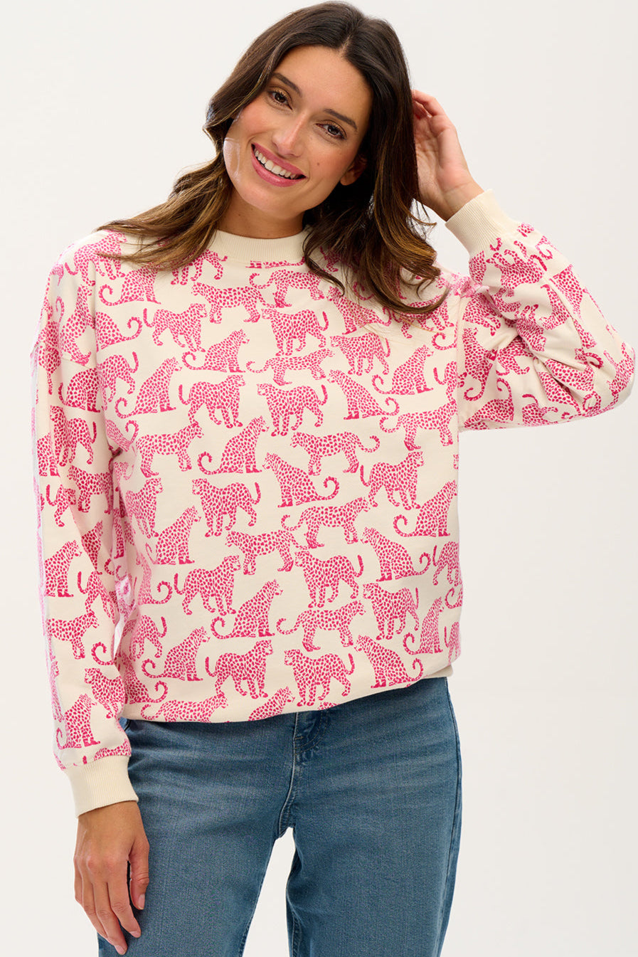 A woman wearing an oversized white sweatshirt with a pink leopard print pattern, paired with blue jeans.